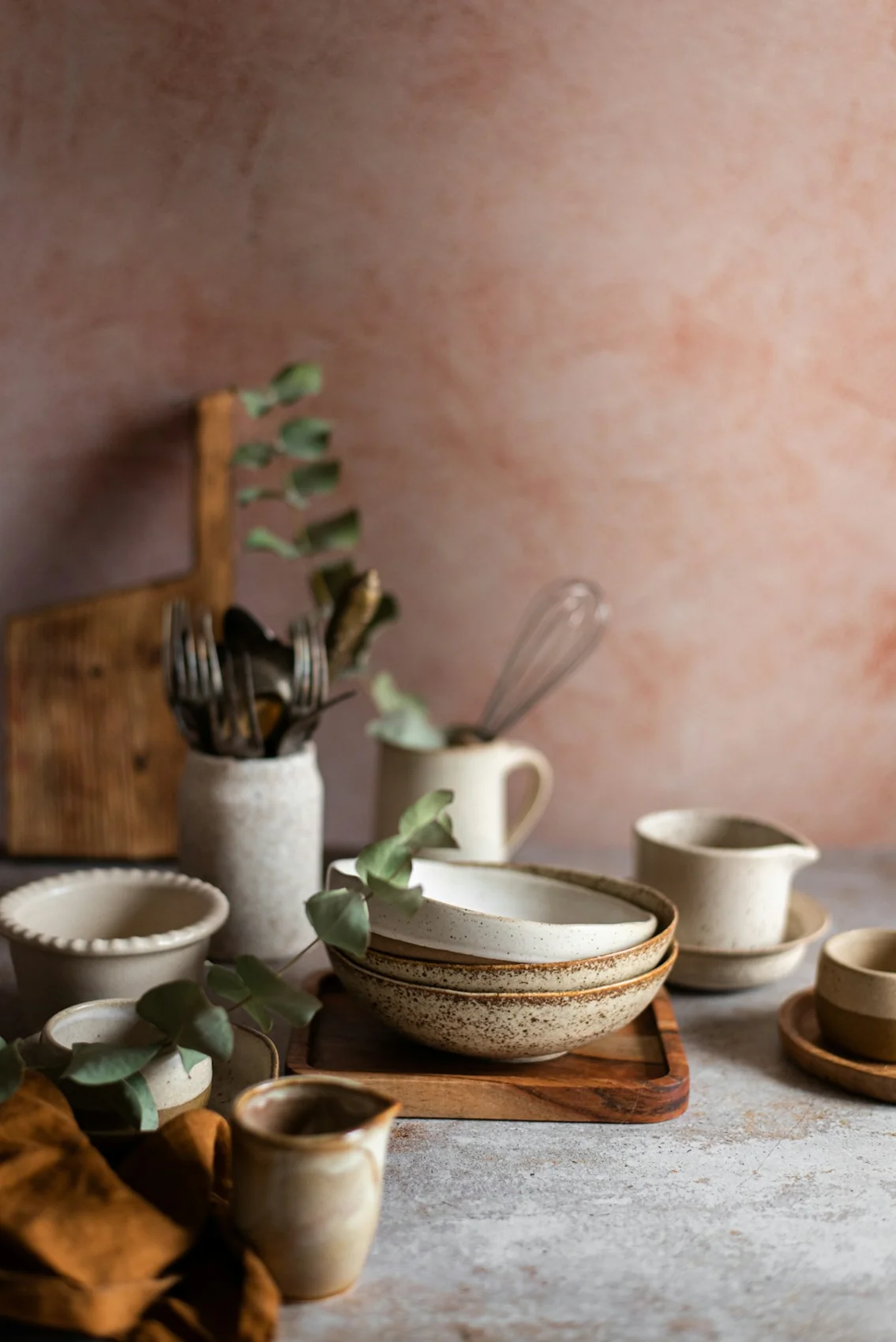 Earth-toned ceramic bowls and mugs styled with wood and eucalyptus
